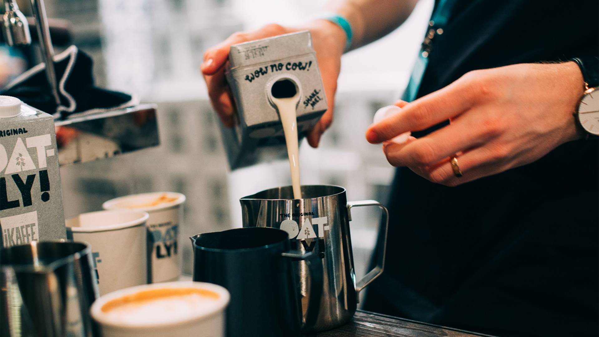 Oatly oat milk being poured into a coffee.